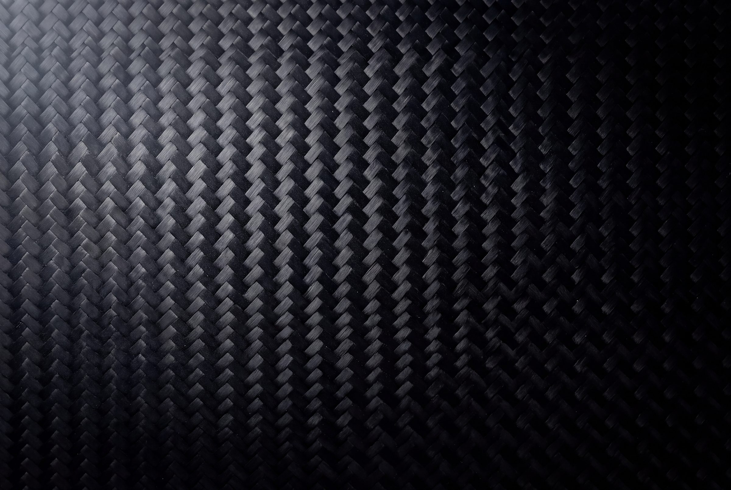 Naviglia vision: macro of a glossy carbon weave, black and graphite, in soft light from the left