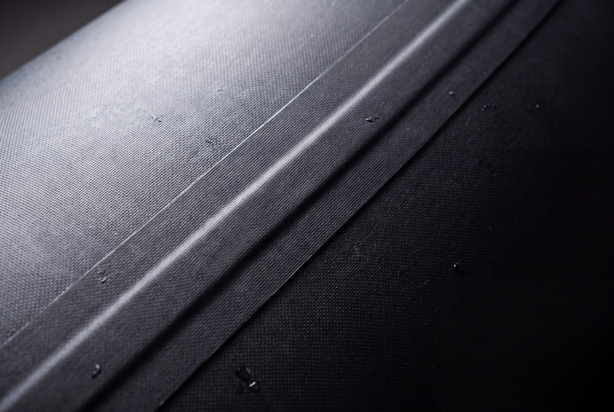 Naviglia vision: macro of the black Hypalon-neoprene fabric of a tube, with the glued seam and a few drops of water