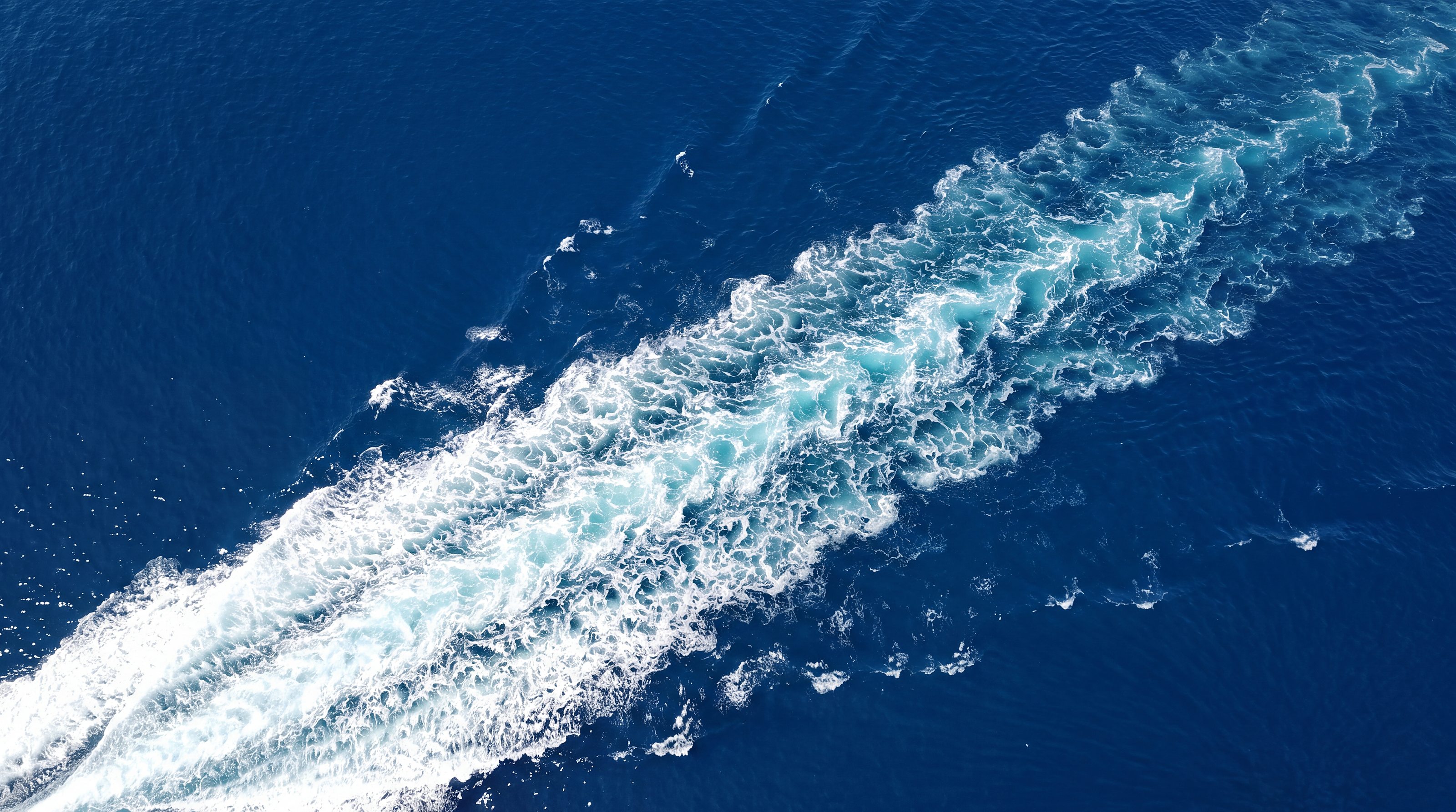 Naviglia vision: white wake of foam on the deep blue sea seen from above, on the diagonal