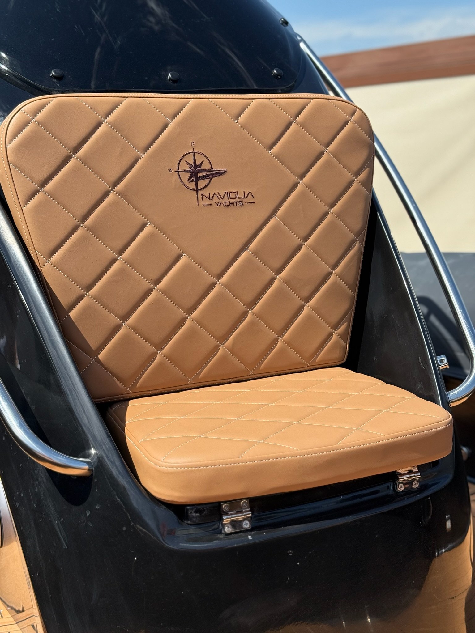 Quilted tan console seat with Naviglia Yachts logo on a black console