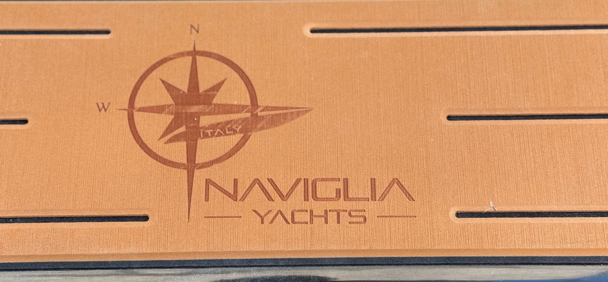 Naviglia Yachts logo with compass rose and ITALY lettering engraved in the teak-effect deck