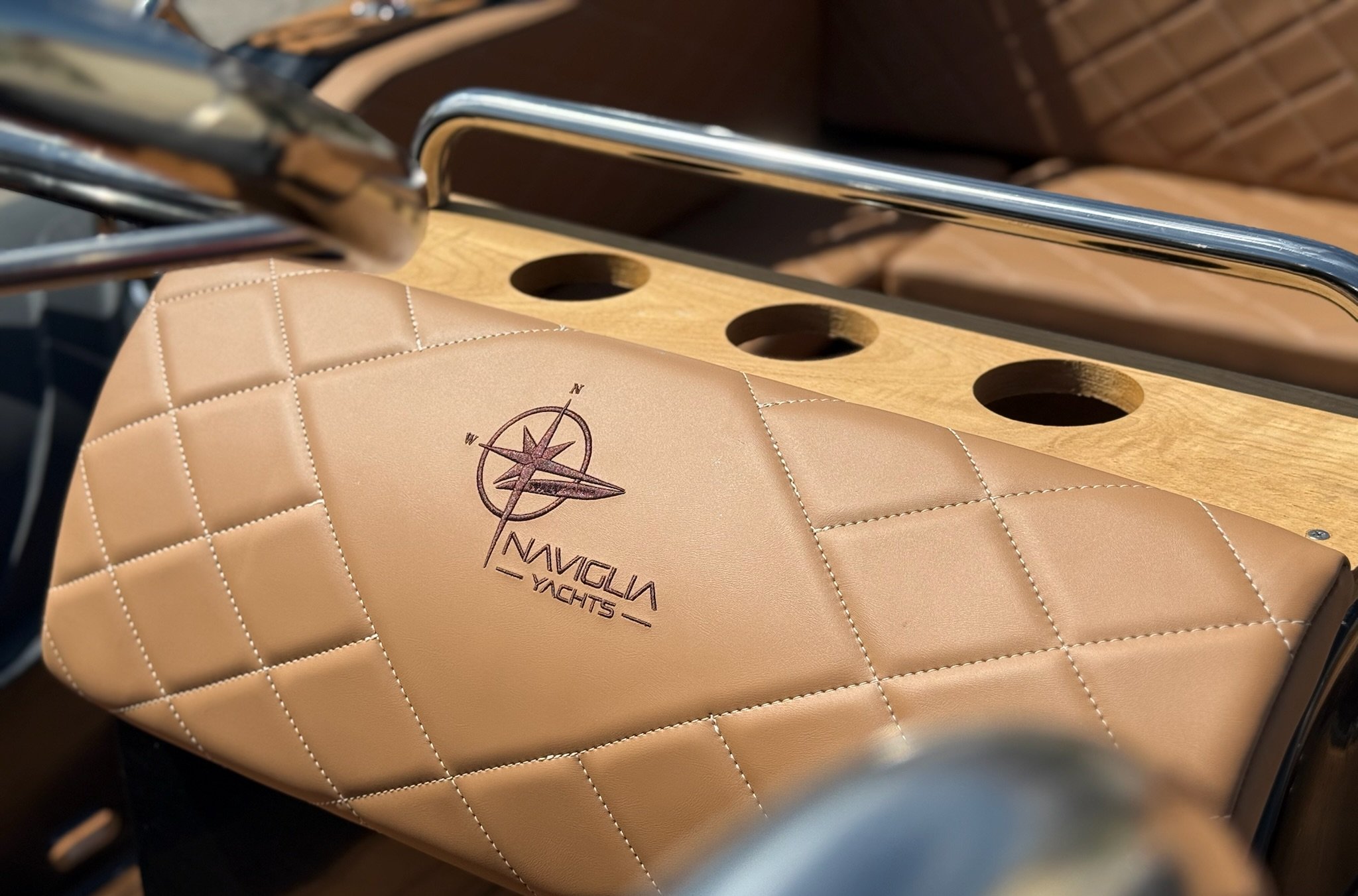 Quilted tan bolster with Naviglia Yachts logo, wooden cup holders and stainless grab rail