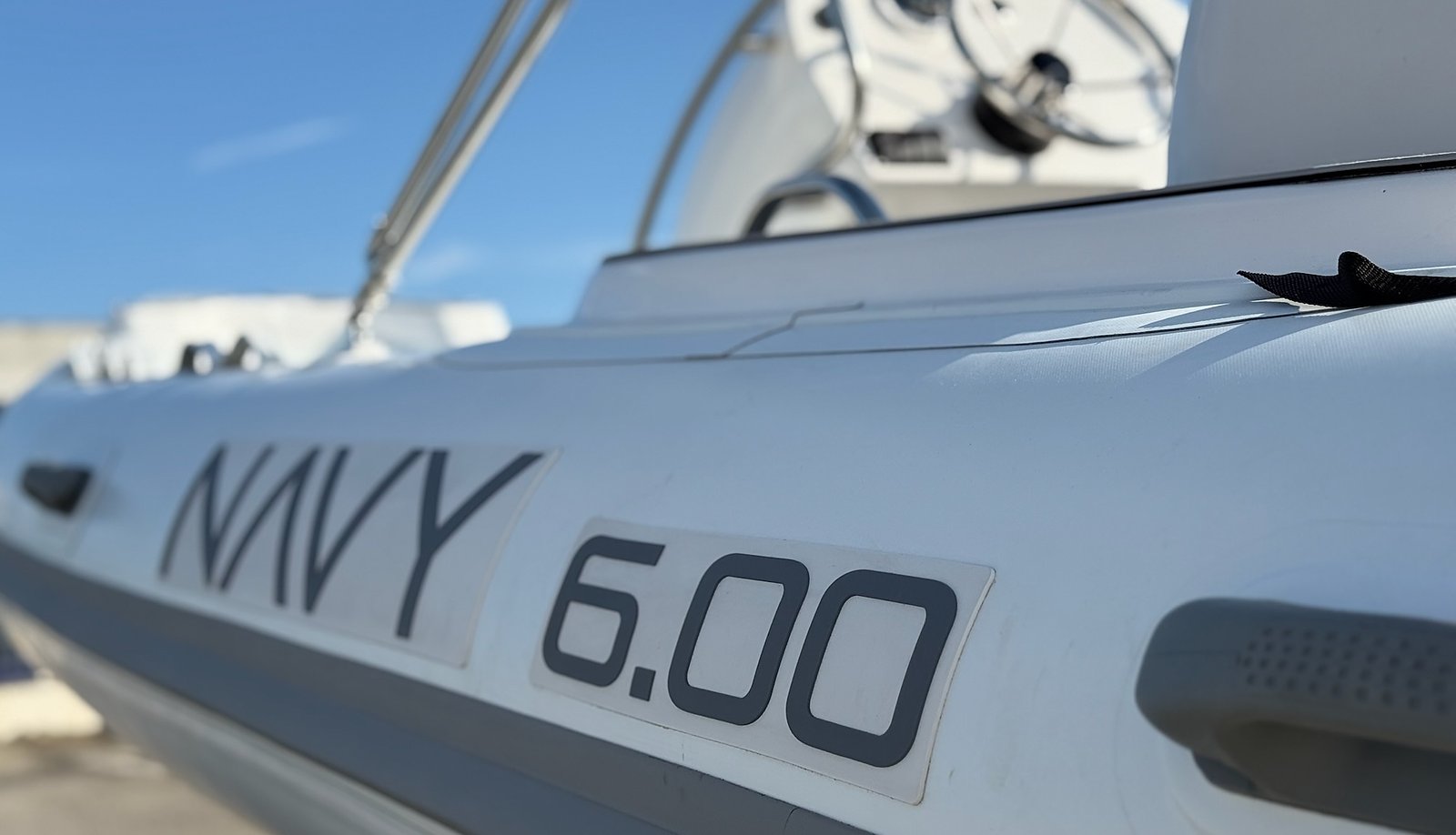 Scritta NAVY 6.00 grigia sul tubolare bianco con maniglia, consolle sfocata e cielo blu