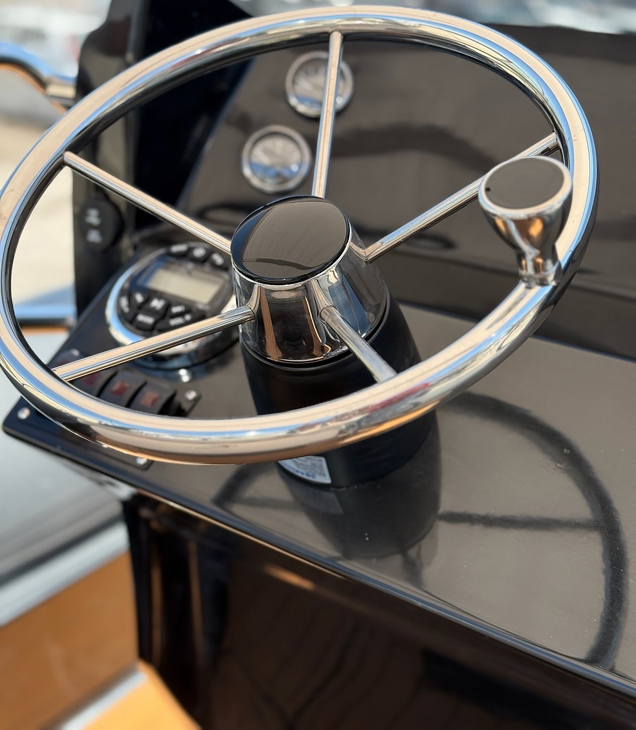 Spoked stainless steering wheel with knob on the gloss black dashboard, instruments blurred, NAVY 7.60