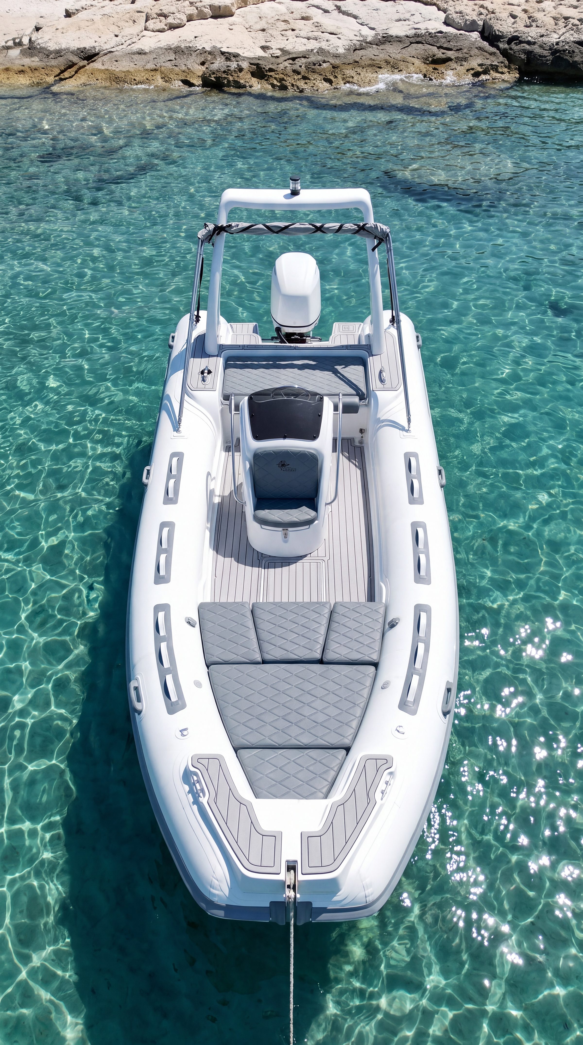 Naviglia vision: the white NAVY 6.00 at anchor seen from above the bow, clear water and pale rocks behind