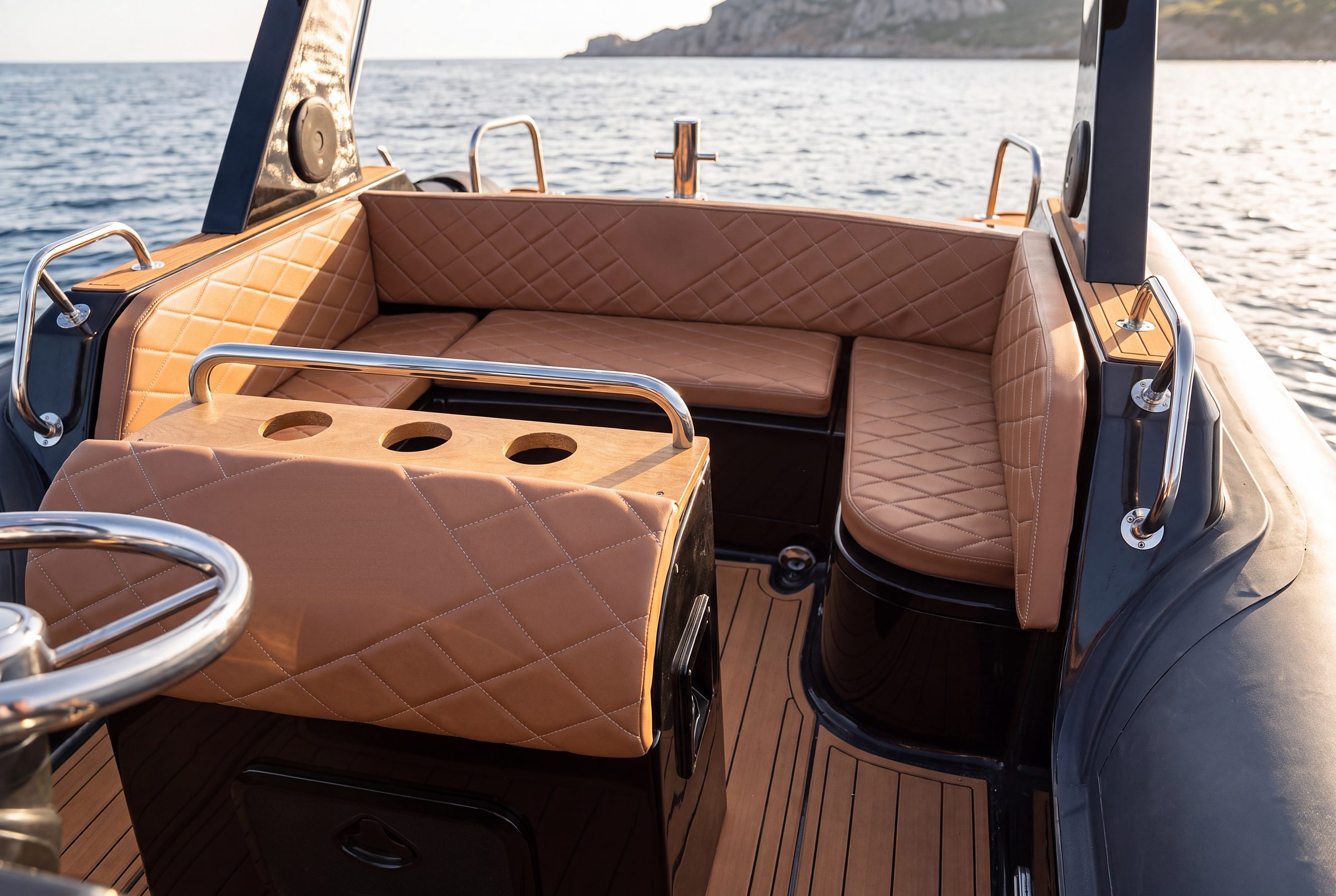 Visione Naviglia: il pozzetto del NAVY 7.60 antracite, divano a U color cuoio trapuntato a rombi, mobile con tre portabicchieri e pagliolo effetto teak, mare sullo sfondo