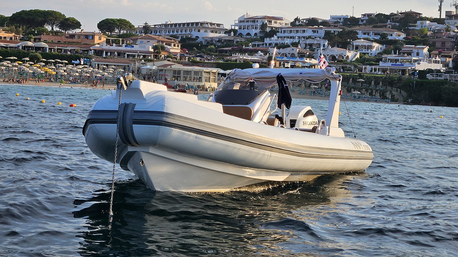NAVY 7.60 visto da prua con catena dell'ancora, spiaggia e case bianche sulla collina
