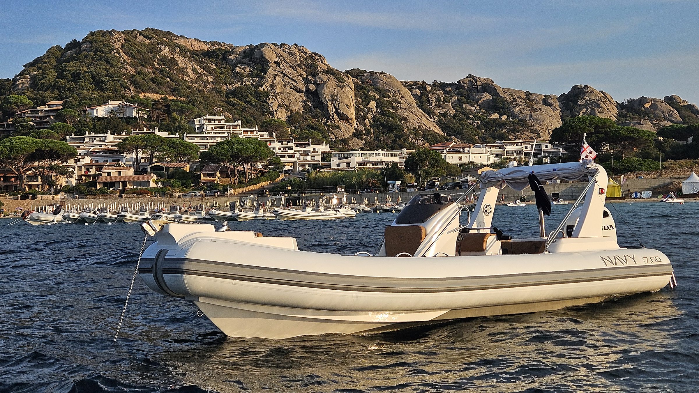 White NAVY 7.60 at anchor, bow three-quarter view, white houses and granite rocks behind