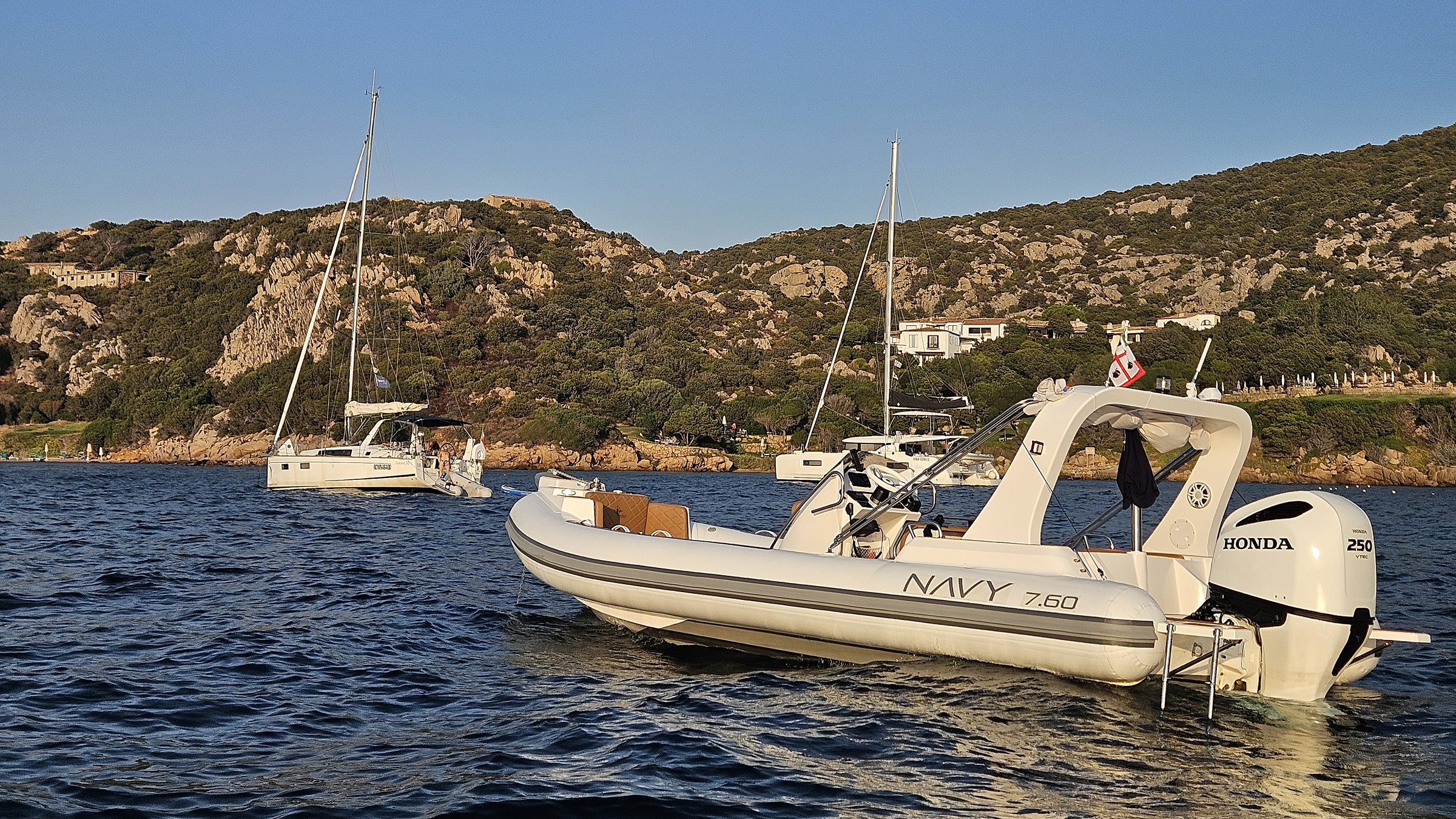 NAVY 7.60 alla fonda in una rada con due barche a vela e collina verde