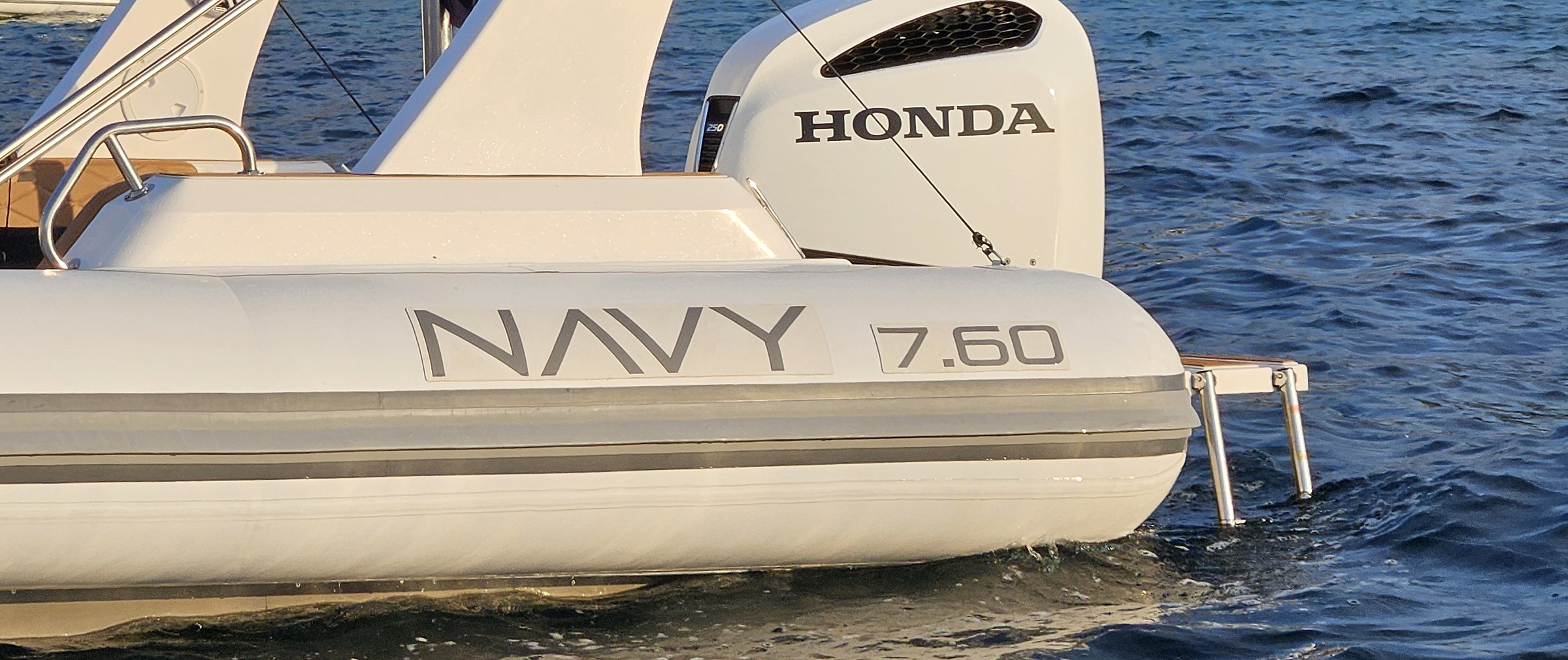 Scritta NAVY 7.60 sul tubolare bianco e fuoribordo Honda in luce dorata, mare blu