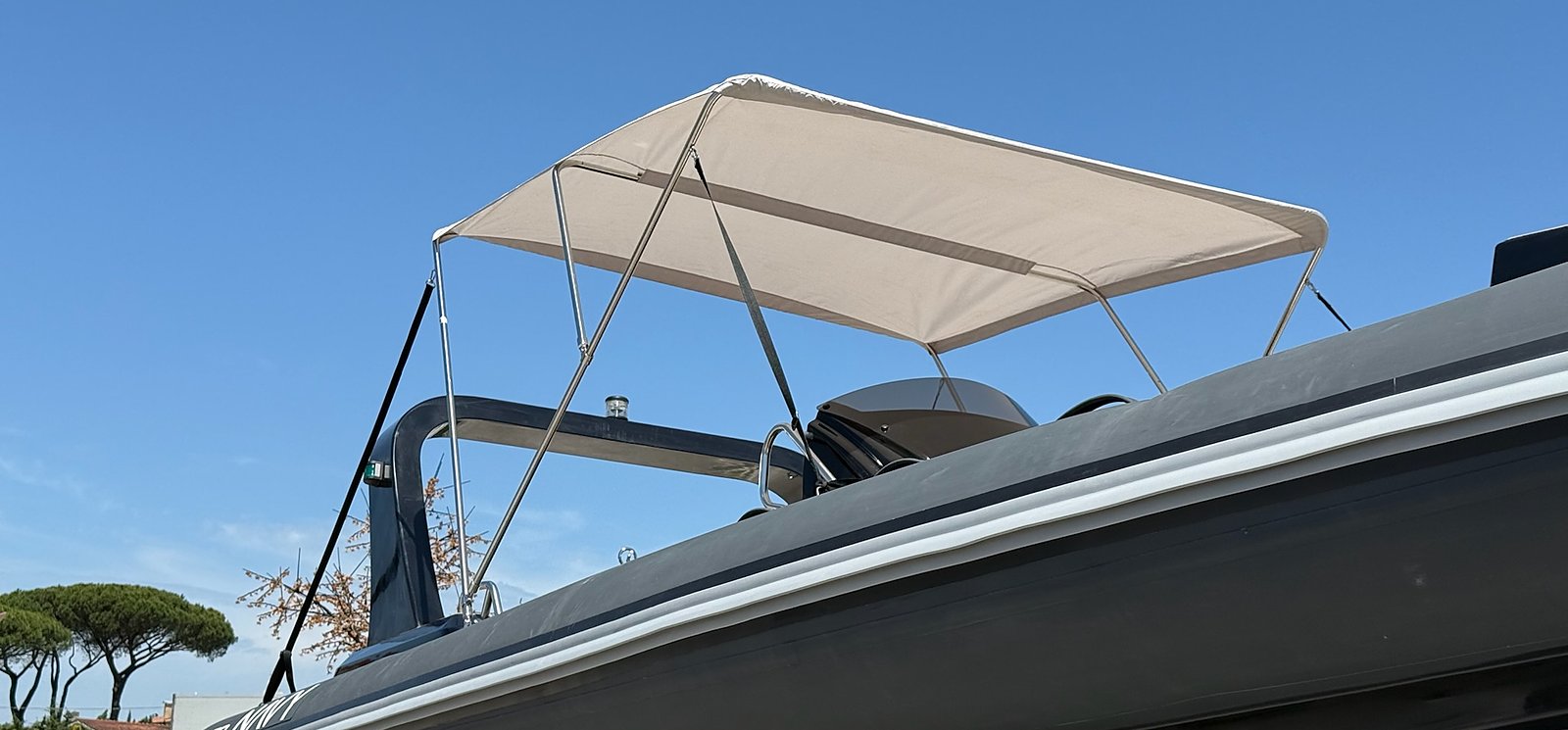 Side of the anthracite NAVY 7.60 from below with bimini open, sky and pine trees